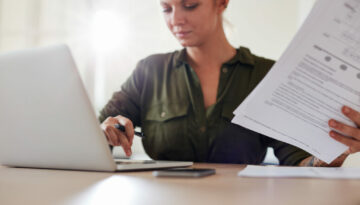 Young woman with documents working on laptop